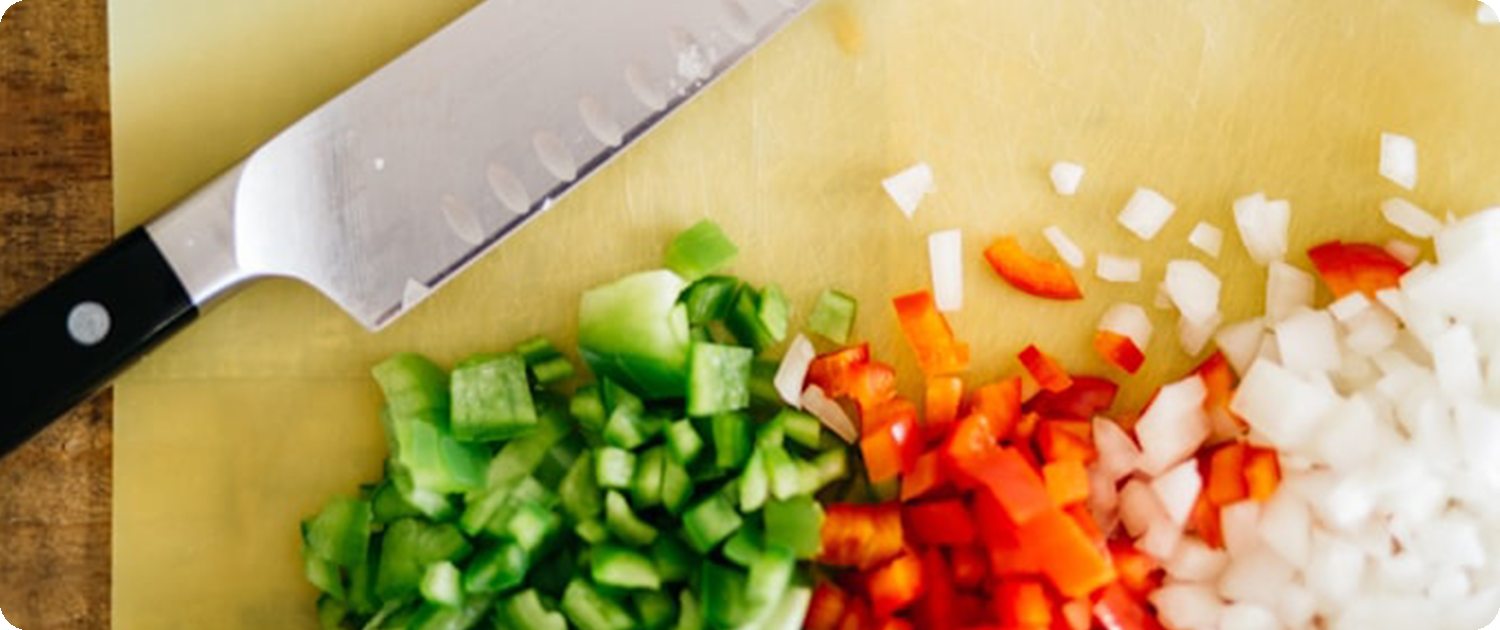WPS Fresh Food Service | Reliable Produce Supply | Restaurants & Kitchens Chopped onions, bell peppers, and celery on a cutting board beside a chef’s knife, representing WPS Fresh Food Service produce offerings.